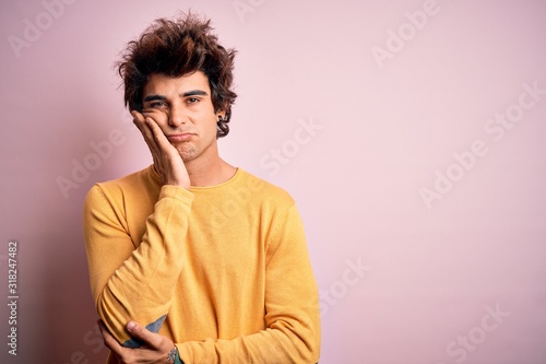 Young handsome man wearing yellow casual t-shirt standing over isolated pink background thinking looking tired and bored with depression problems with crossed arms. © Krakenimages.com