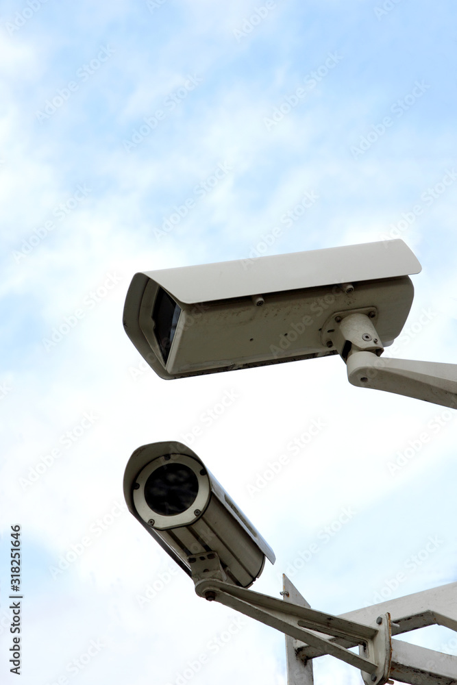 Two surveillance cameras hanging on the street on a pole on the background of the sky the sky Two surveillance cameras hanging on the street on a pole on the background of the sky the sky