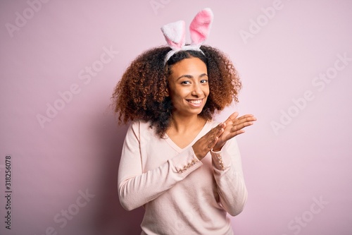 Young african american woman with afro hair wearing bunny ears over pink background clapping and applauding happy and joyful, smiling proud hands together