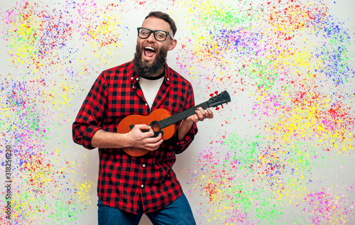 Handsome hipster guy plays ukulele guitar isolate over colorful background photo