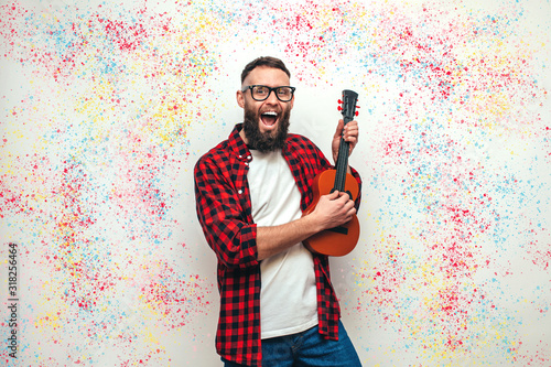 Handsome hipster guy plays ukulele guitar isolate over colorful background photo