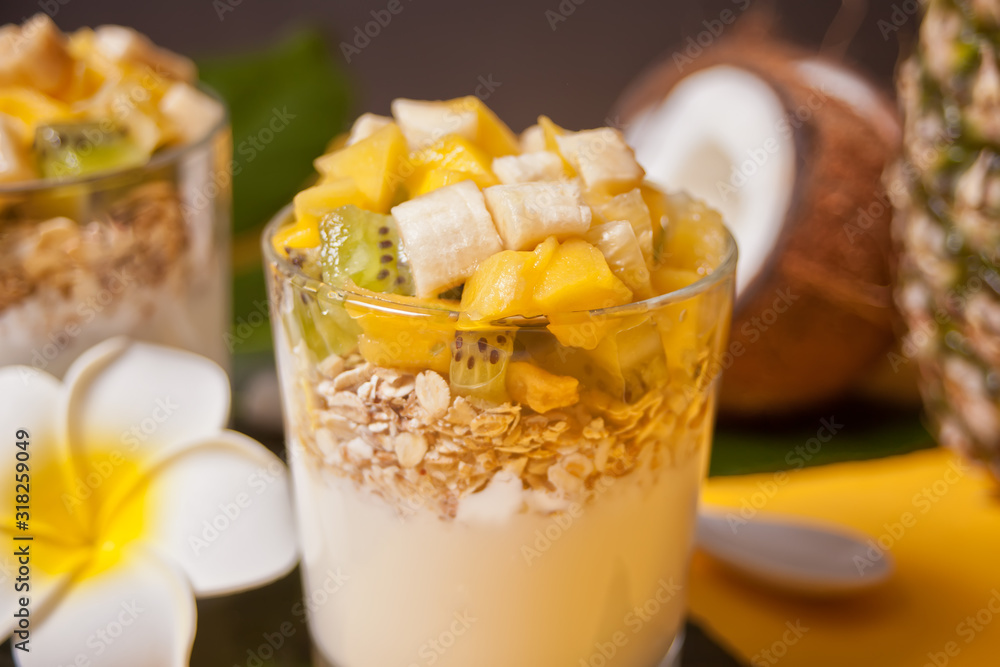 Exotic tropical fruit salad with muesli and yogurt in a glass with pineapple and coconut on the background.