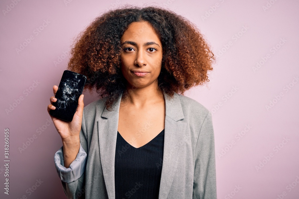 Young african american woman with afro hair holding cracked and broken smartphone screen with a confident expression on smart face thinking serious Young african american woman with afro hair holding cracked and broken smartphone screen with a confident expression on smart face thinking serious
