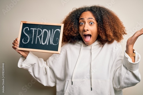 Young african american woman with afro hair holding blackboard with strong message very happy and excited, winner expression celebrating victory screaming with big smile and raised hands