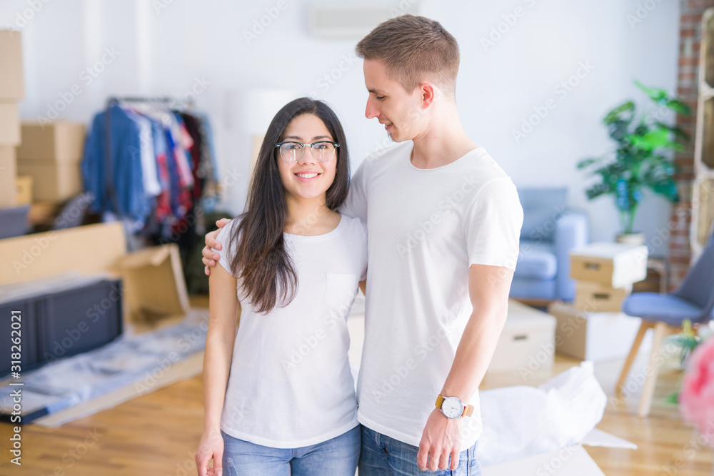 Fototapeta premium Young beautiful couple standing at new home around cardboard boxes