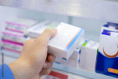 At the chemist, Medicines and healthcare products arranged in shelves, Pharmacist holding medicine boxes of drugs in pharmacy drugstore for prescribe to patient. Pharmaceutical prescribing concept.