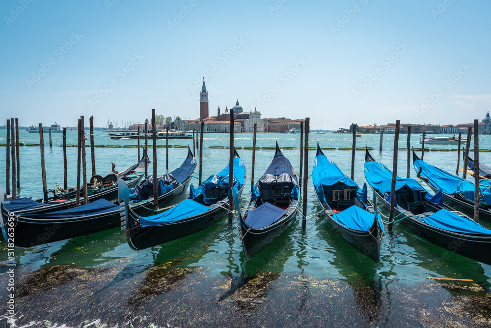 Gondolas on the Grand Canal pier in Venice. San Giorgio Maggiore Island background. The row of  beautiful bright colored Venetian gondolas mooring on berth. Jetty. Panoramic view of  Venice lagoon.