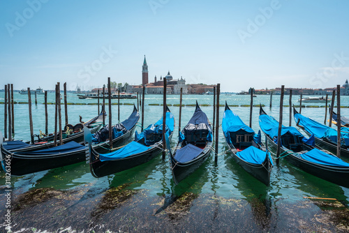 Gondolas on the Grand Canal pier in Venice. San Giorgio Maggiore Island background. The row of  beautiful bright colored Venetian gondolas mooring on berth. Jetty. Panoramic view of  Venice lagoon. © GenоМ.