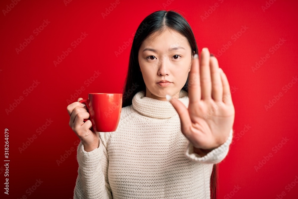 Young asian woman drinking a cup of hot coffee over isolated red background with open hand doing stop sign with serious and confident expression, defense gesture Young asian woman drinking a cup of hot coffee over isolated red background with open hand doing stop sign with serious and confident expression, defense gesture