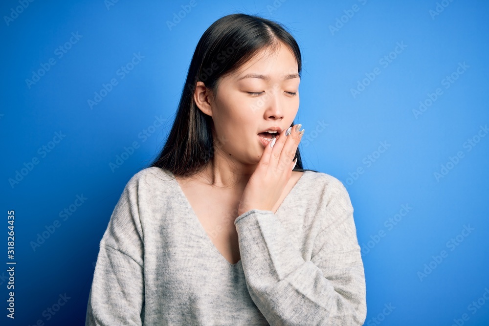 Young beautiful asian woman wearing casual sweater standing over blue isolated background bored yawning tired covering mouth with hand. Restless and sleepiness. Young beautiful asian woman wearing casual sweater standing over blue isolated background bored yawning tired covering mouth with hand. Restless and sleepiness.