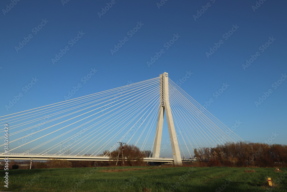 Rzeszow, Poland - 9 9 2018: Suspended road bridge across the Wislok River. Metal construction technological structure. Modern architecture. A white cross on a blue background is a symbol of the city Rzeszow, Poland - 9 9 2018: Suspended road bridge across the Wislok River. Metal construction technological structure. Modern architecture. A white cross on a blue background is a symbol of the city