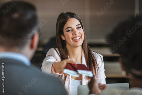 Beautiful female travel agent is working with clients in office and offering them tours. Young woman smiling and giving tickets, passport with visa to tourists. Close-up photo