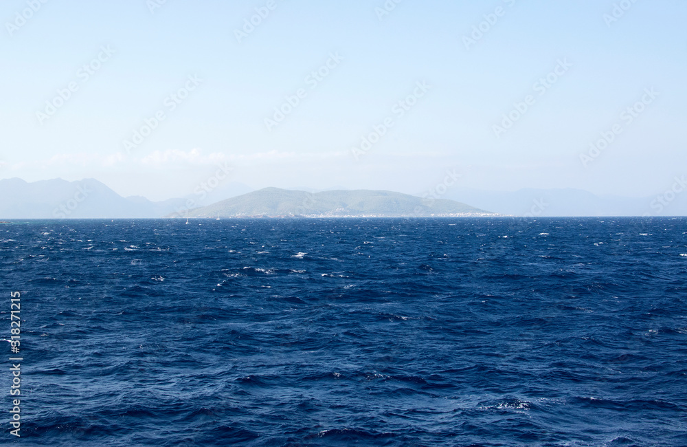 Dark blue sea against a background of blue sky and barely visible mountains on the horizon. Sea with small waves.