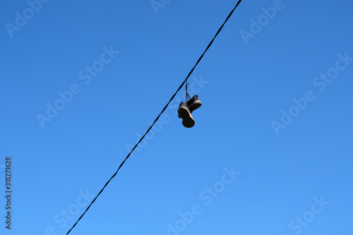 A pair of old sneakers hanging on wires against a blue sky.