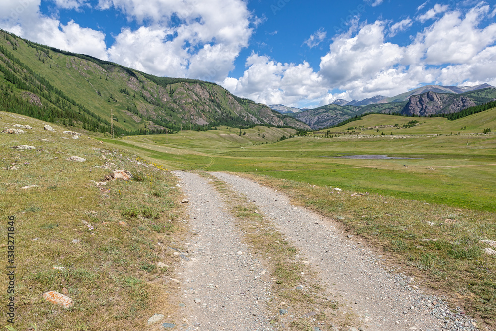 Beautiful dirt road in the mountains of Altai, against the backdrop of mountains and clouds.