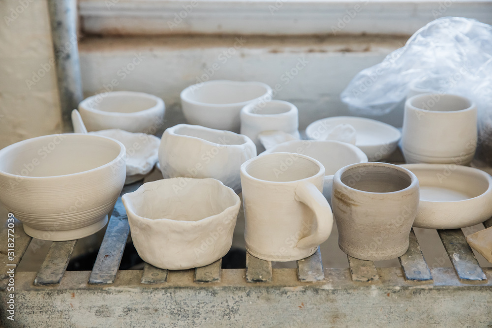 A shelf full of unfinished clay ceramic pottery pieces that are waiting to be fired in a kiln A shelf full of unfinished clay ceramic pottery pieces that are waiting to be fired in a kiln