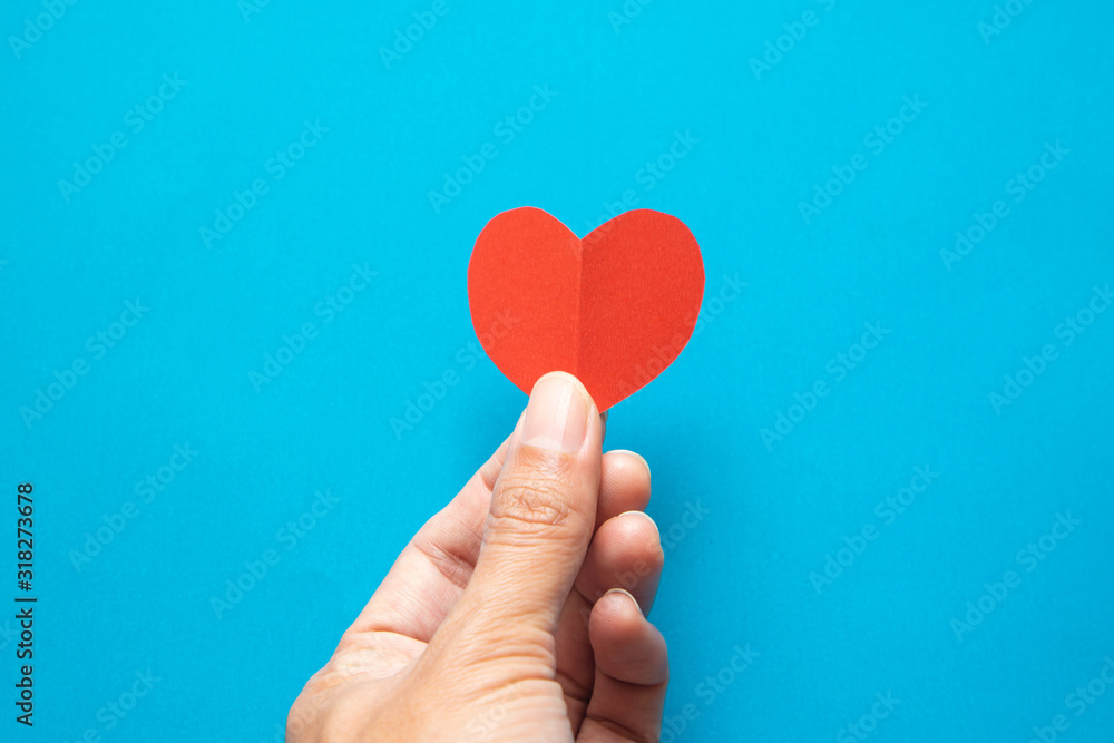 Hand holding red heart paper on blue background