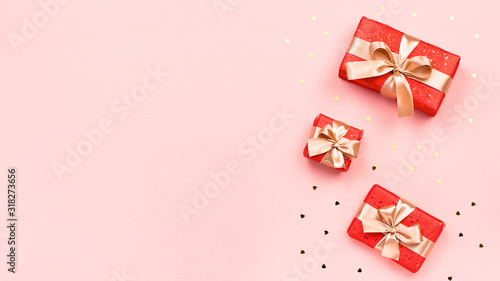 Creative Valentine's Day greeting card with red decorations and gift boxes, golden heart confetti on pink background, copy space, top view