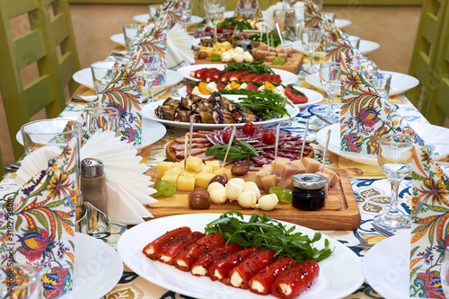 Beautiful served table for wedding or other celebration in restaurant with dishes of cheese, sausage, vegetables (eggplant, tomatoes, bell pepper)