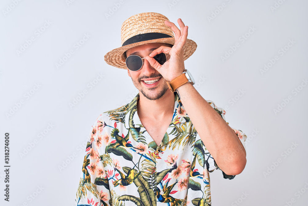 Young handsome man wearing Hawaiian shirt and summer hat over isolated background doing ok gesture with hand smiling, eye looking through fingers with happy face. Young handsome man wearing Hawaiian shirt and summer hat over isolated background doing ok gesture with hand smiling, eye looking through fingers with happy face.