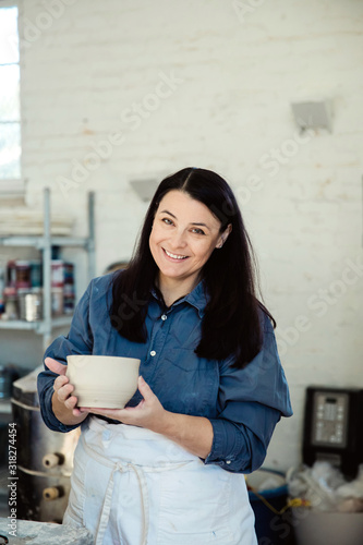 smiling Creative Pottery Cermanic female artist holding a piece of unfinished clay pottery in an art loft studio photo