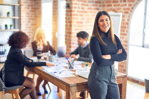 Group of business workers working together. Young beautiful woman standing smiling happy looking at the camera at the office