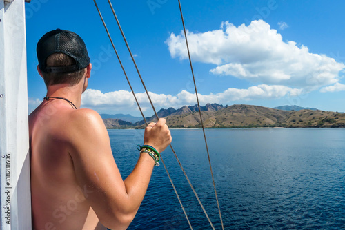 A man leaning against the mast of a sail boat enjoying beautiful island view in Komodo National Park, Flores, Indonesia. Man is enjoying the beauty of the nature. Calm sea, perfect weather for sailing © Chris