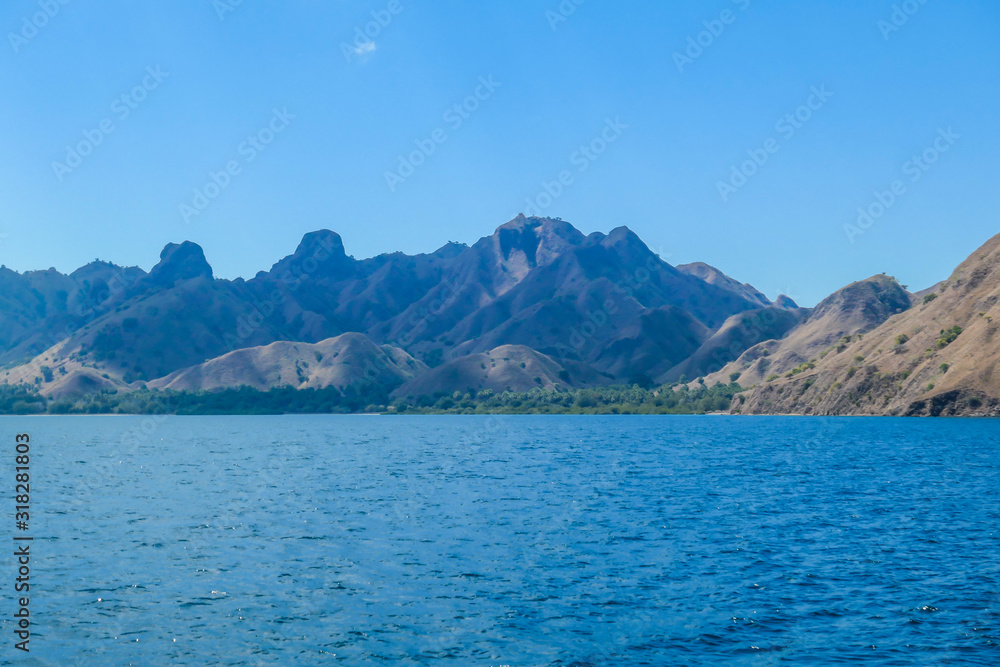 A view on idyllic island in Komodo National Park, Indonesia. There are few clouds above the island. Calm and clear surface of the sea. Island hoping. Perfect day for sailing