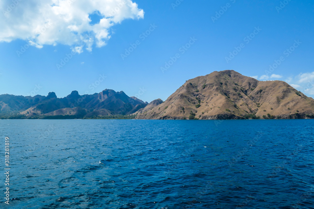 A view on idyllic island in Komodo National Park, Indonesia. There are few clouds above the island. Calm and clear surface of the sea. Island hoping. Perfect day for sailing