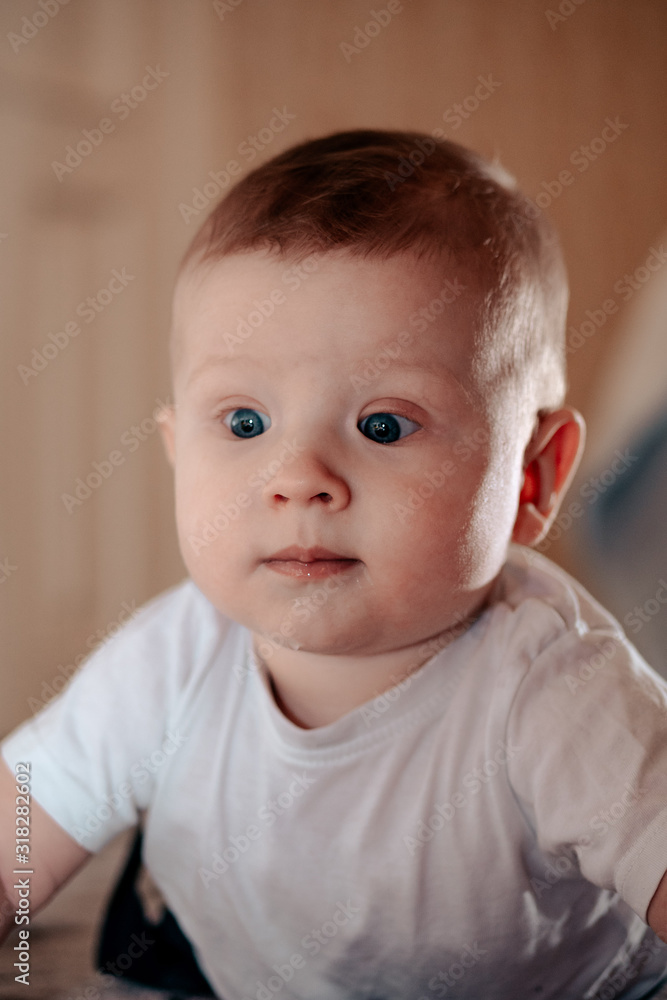 The kid is very surprised and amazed. The baby was thinking about something. The boy lies on his stomach on the floor. A little boy is playing on the floor.