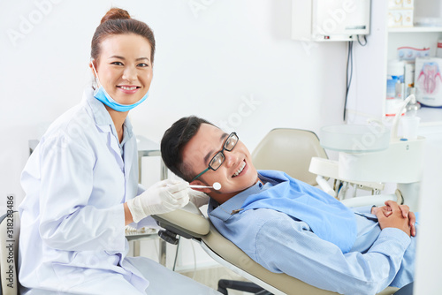 Horizontal portrait of professional dental surgeon sitting close to her cheerful patient smiling on camera