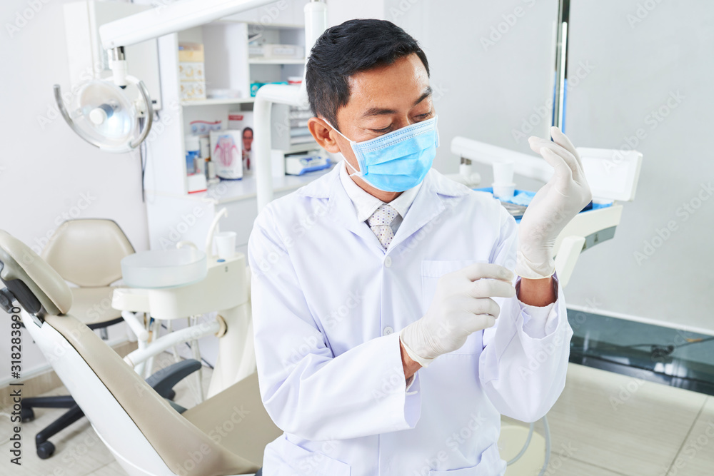 Dentist with mask on face putting on protective gloves for starting his work, horizontal portrait Dentist with mask on face putting on protective gloves for starting his work, horizontal portrait