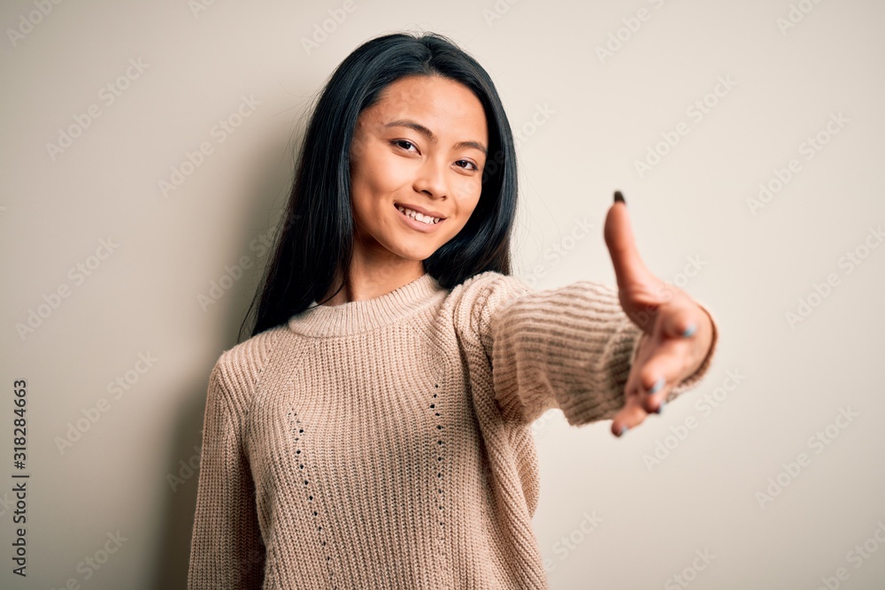 Young beautiful chinese woman wearing casual sweater over isolated white background smiling friendly offering handshake as greeting and welcoming. Successful business. Young beautiful chinese woman wearing casual sweater over isolated white background smiling friendly offering handshake as greeting and welcoming. Successful business.