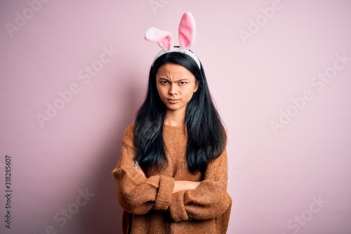 Young beautiful chinese woman wearing bunny ears standing over isolated pink background skeptic and nervous, disapproving expression on face with crossed arms. Negative person.