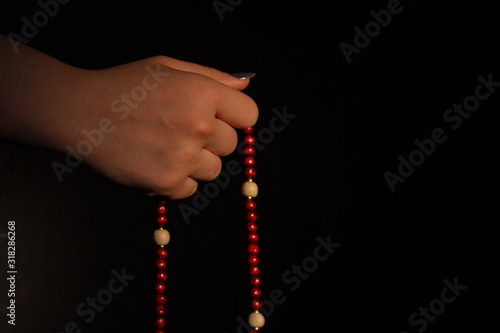 Woman's holding red rosary. Close-up. Black background.