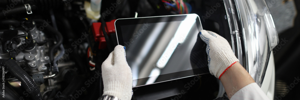 Obraz premium Close-up of special digital tablet used for automobile checkup and fixing damaged car parts. Mechanic in white gloves and working outfit in service station. Copy space on screen. Automotive check
