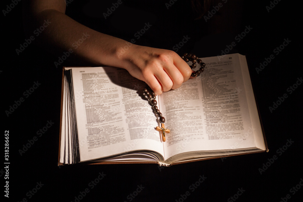 Fototapeta premium Female hand holding opened holy bible and crucifix. Book pages with religious text, reading word of God.
