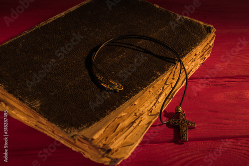 Very old ancient holy bible and neckalce cross. Worn vintage retro book on red wood. photo