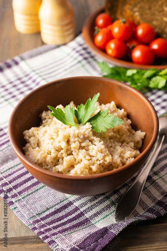 Healthy vegetarian breakfast with wheat porridge in a bowl, bread, tomatoes and parsley on wooden rustic table Healthy vegetarian breakfast with wheat porridge in a bowl, bread, tomatoes and parsley on wooden rustic table