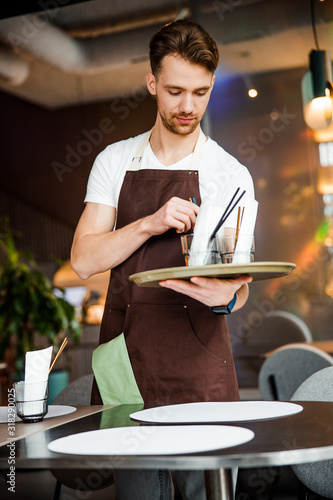 Calm cute waiter lays the table in cafe photo
