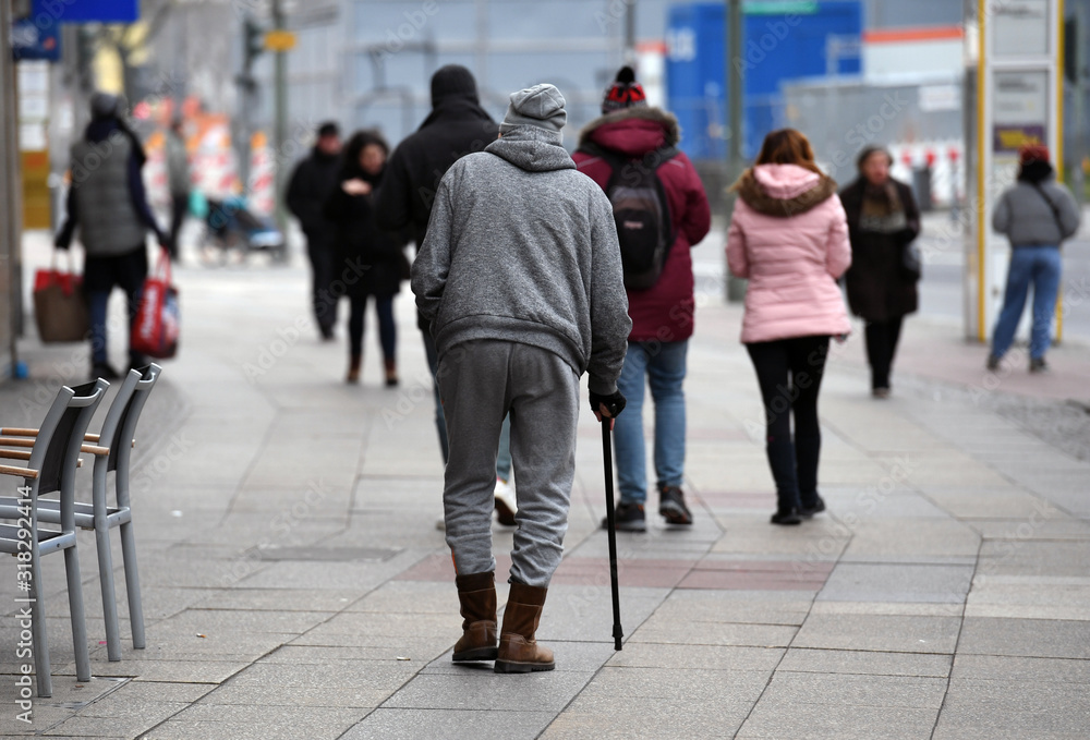 An old man with a sports suit and a walking stick goes for a walk on the Kuhdamm in Berlin Germany on a cold winter day