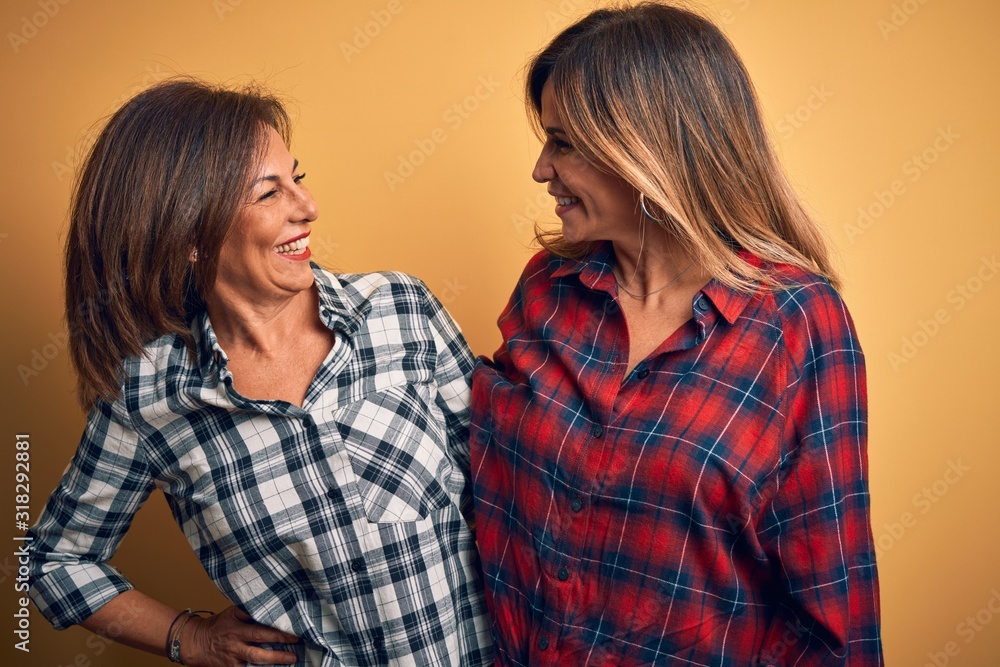 Middle age beautiful couple of sisters smilling happy and confident. Standing with smile on face hugging over isolated yellow background Middle age beautiful couple of sisters smilling happy and confident. Standing with smile on face hugging over isolated yellow background