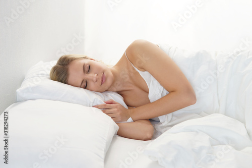 Young woman lying in the bed. Beautiful blond sleeping girl. Morning in the bedroom  daylight from the window. Health and rest.
