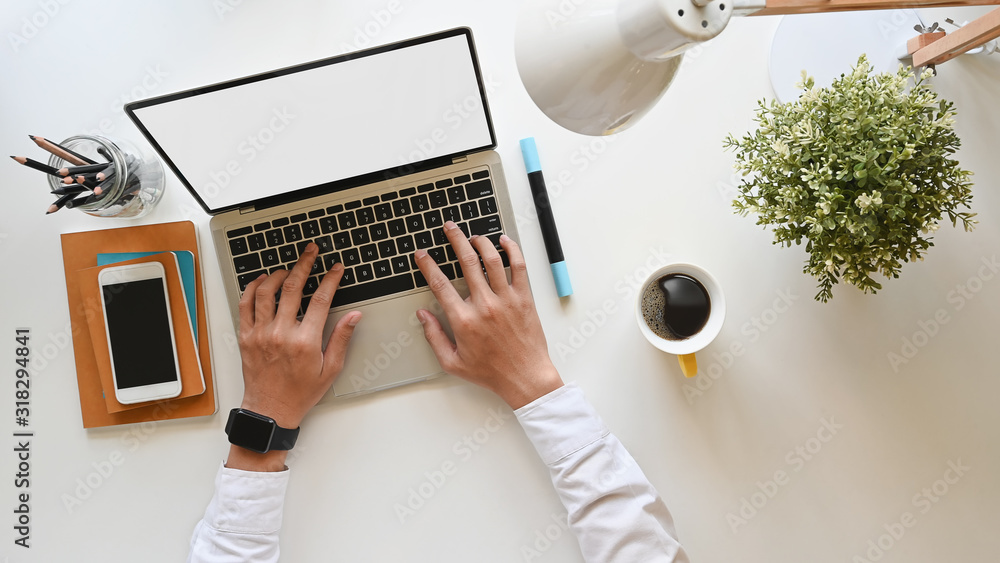 Top view of businessman typing on white blank screen laptop at the modern working desk. Including working equipment on desk. - obrazy, fototapety, plakaty 