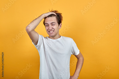 Emotional man in white t-short yellow background grimace discontent. Holding hand to hair