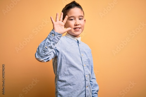 Young little boy kid wearing elegant shirt standing over yellow isolated background showing and pointing up with fingers number five while smiling confident and happy.