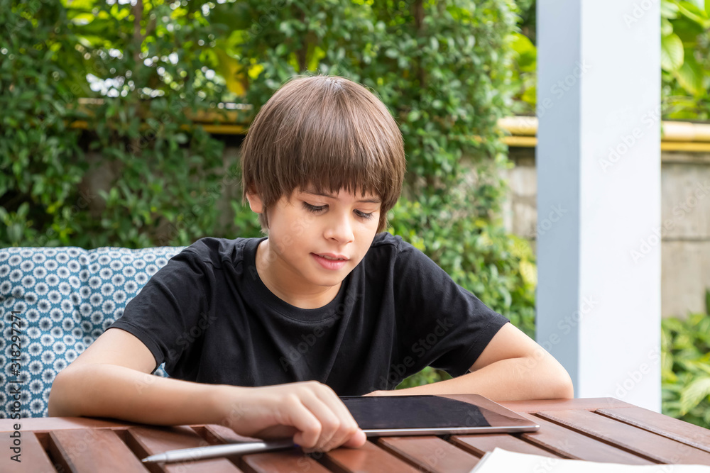 Cute boy using tablet while doing homework in garden at home Cute boy using tablet while doing homework in garden at home