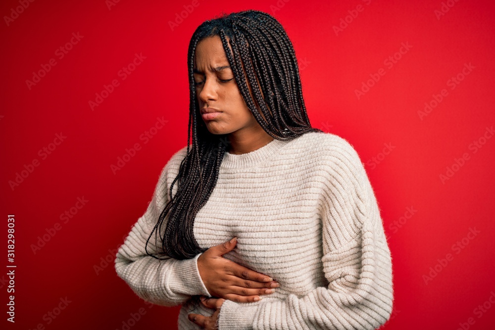 Young african american woman wearing casual winter sweater over red isolated background with hand on stomach because indigestion, painful illness feeling unwell. Ache concept. Young african american woman wearing casual winter sweater over red isolated background with hand on stomach because indigestion, painful illness feeling unwell. Ache concept.