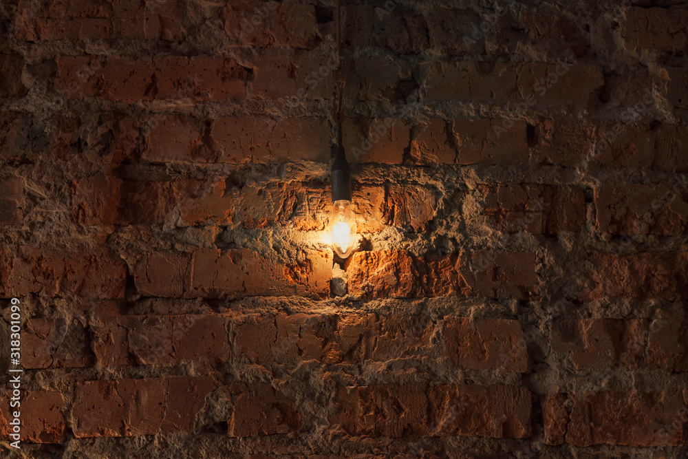 A bright light bulb shines on the background of an old brick wall in the house in the evening. Background for inscriptions in vintage style.