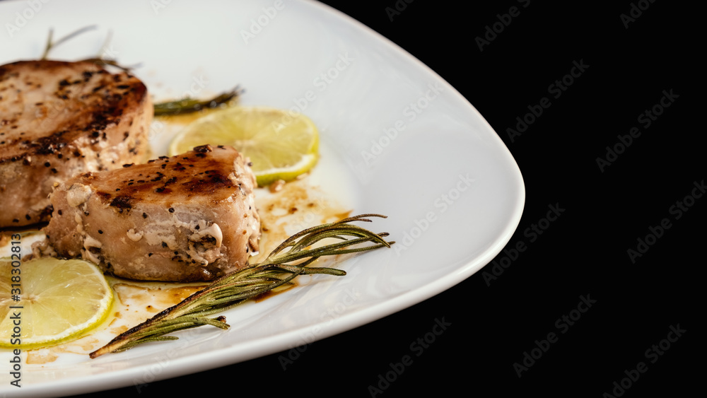 Freshly cooked grilled tuna steak with rosemary, lime, lemon on white plate. Seared tuna fish, roasted. Top view from above horizontal, close up, closeup